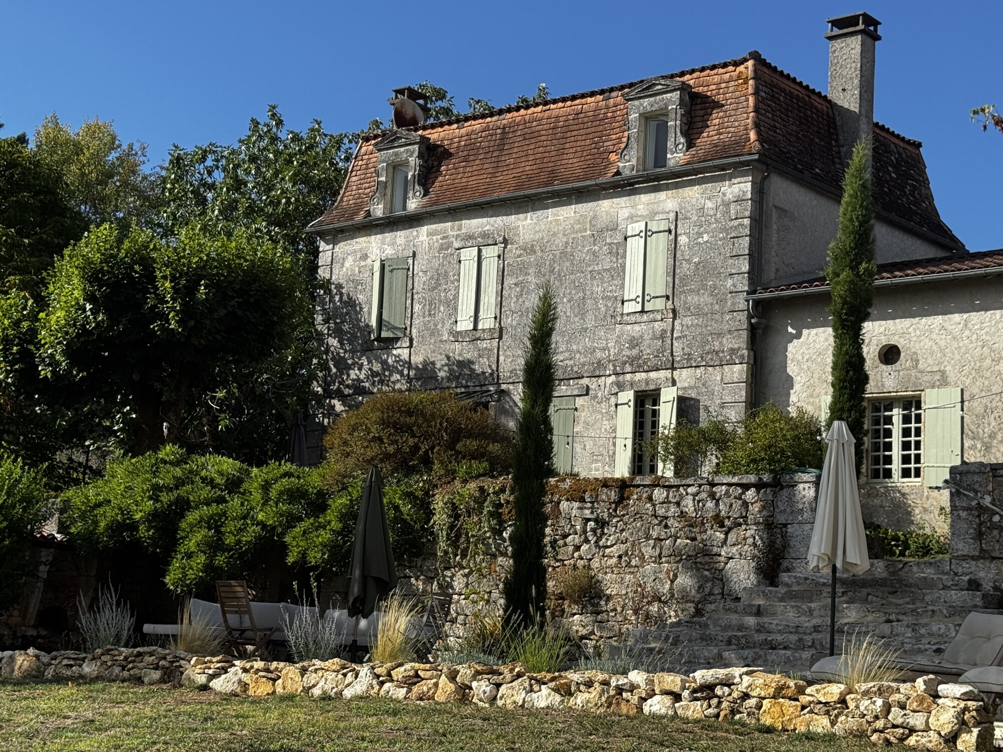 The historic façade of Maison Rivers framed by mature planting and old stone walls