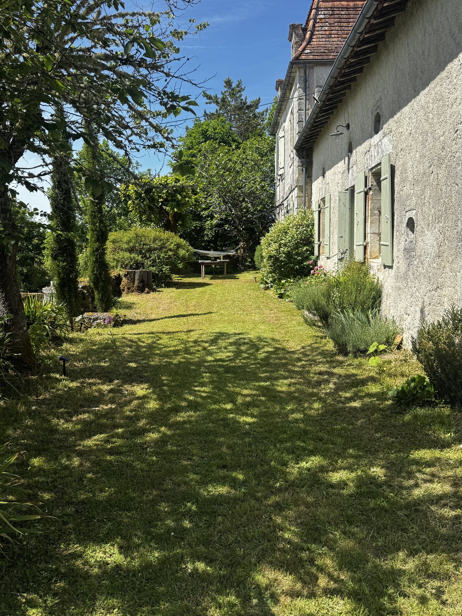 A quiet lawn and garden beside the stone buildings of Maison Rivers