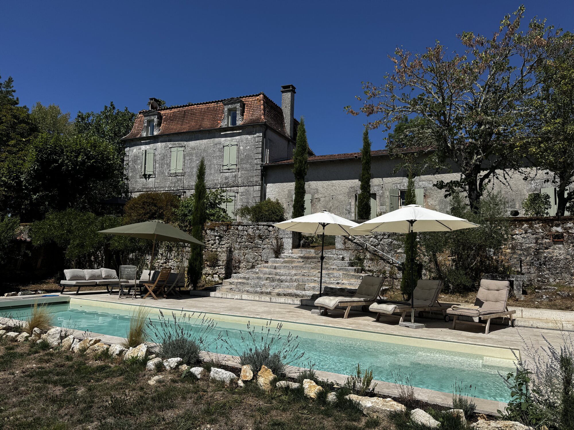 The pool terrace beneath parasols in front of Maison Rivers on a bright summer day