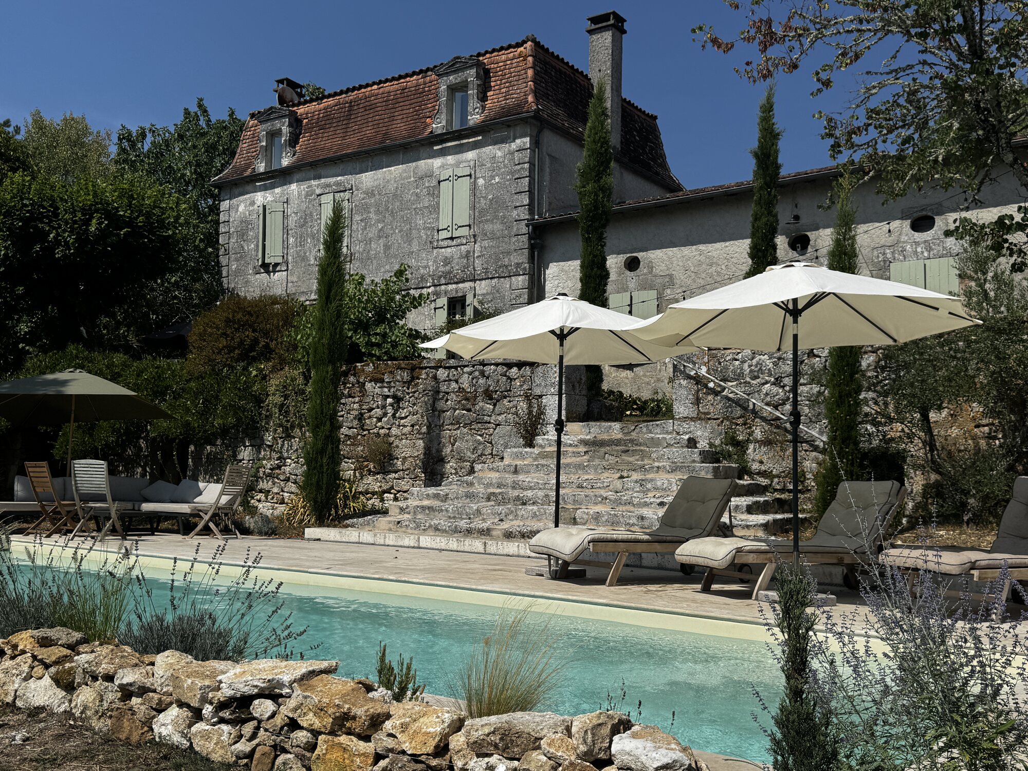 Pool loungers and parasols arranged beneath the historic farmhouse and stone terrace