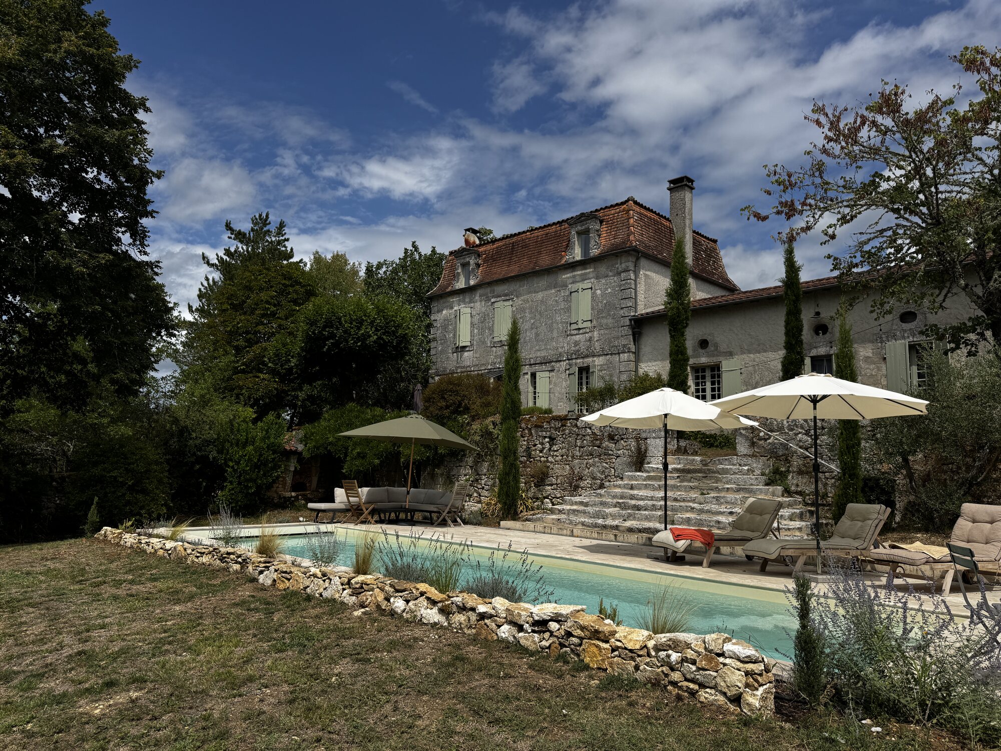 Wide view of the pool and farmhouse under a blue Dordogne sky